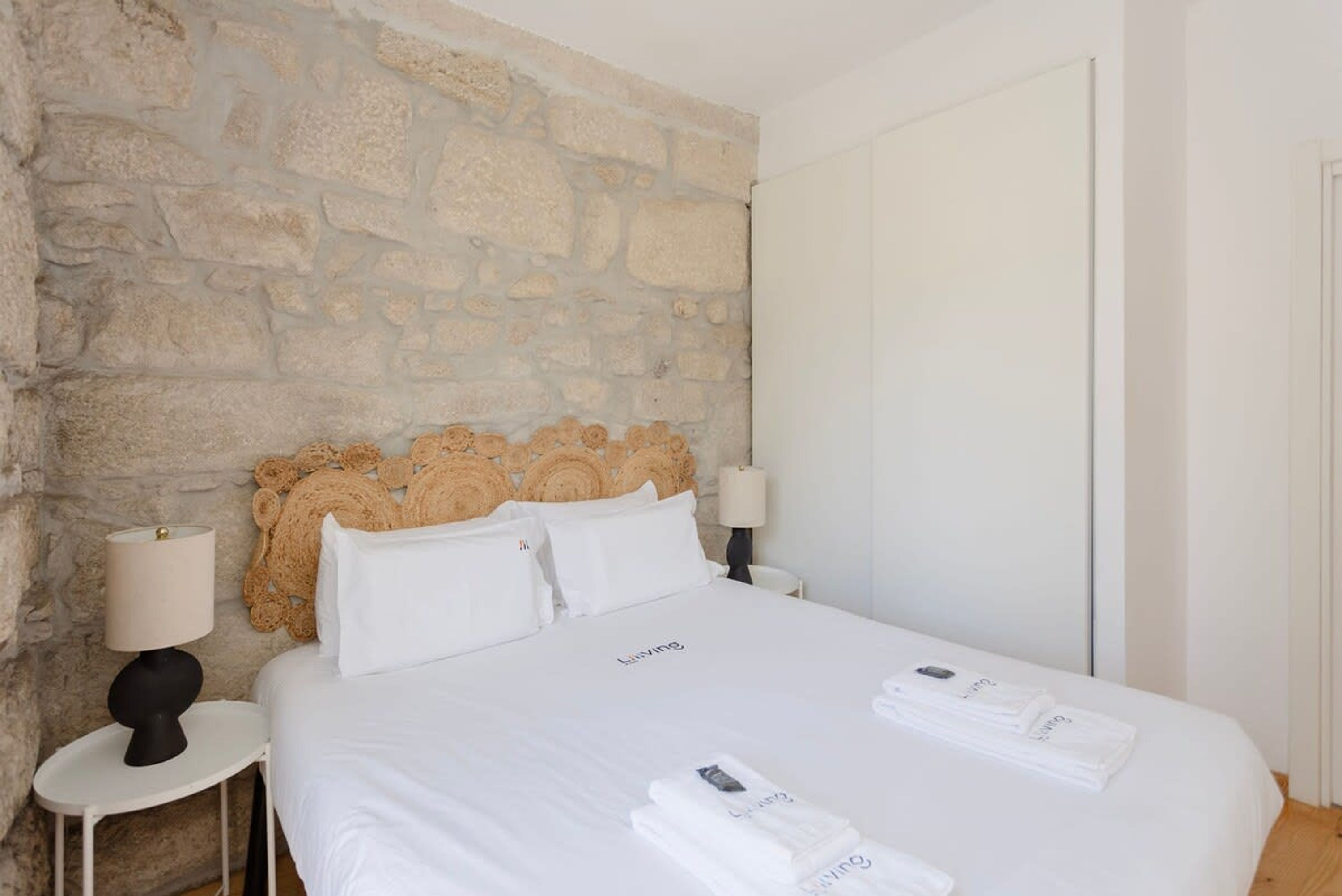 Ett hotellrum med en vägg av natursten, en säng med vita sängkläder, två sänglampor och en sänggavel med ett utskuret mönster.