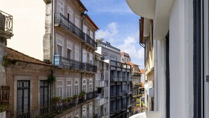 A narrow street with buildings featuring traditional European architecture, including balconies with plants and a visible storefront with signage. - Liiiving in Gaia - Casa da Vinha Apartment VI (Vila Nova de Gaia)