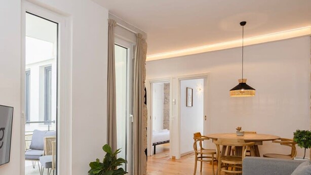 A modern living room with a wooden floor, a grey sofa, a dining table with chairs, and a hanging pendant light. - Liiiving in Gaia - Casa da Vinha Apartment VI (Vila Nova de Gaia)