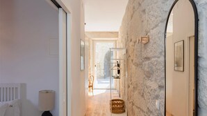 Un couloir avec un mur en pierre, un plancher en bois, un lit, une lampe et un miroir.