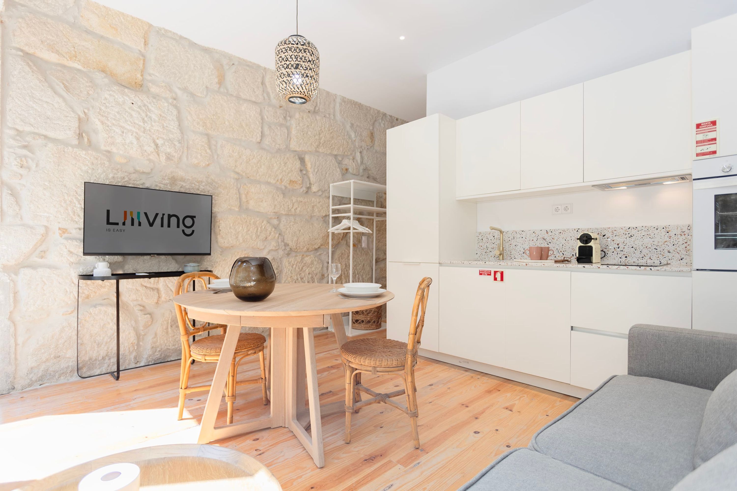 Eine moderne Küche mit weißen Schränken, einer Steinwand und einem Essbereich mit Holztisch und Korbstühlen.