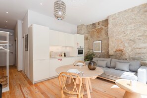 A modern kitchen with white cabinets, a dining table with chairs, and a stone accent wall. - Liiiving In Gaia - The Wine Side XII (Vila Nova de Gaia)