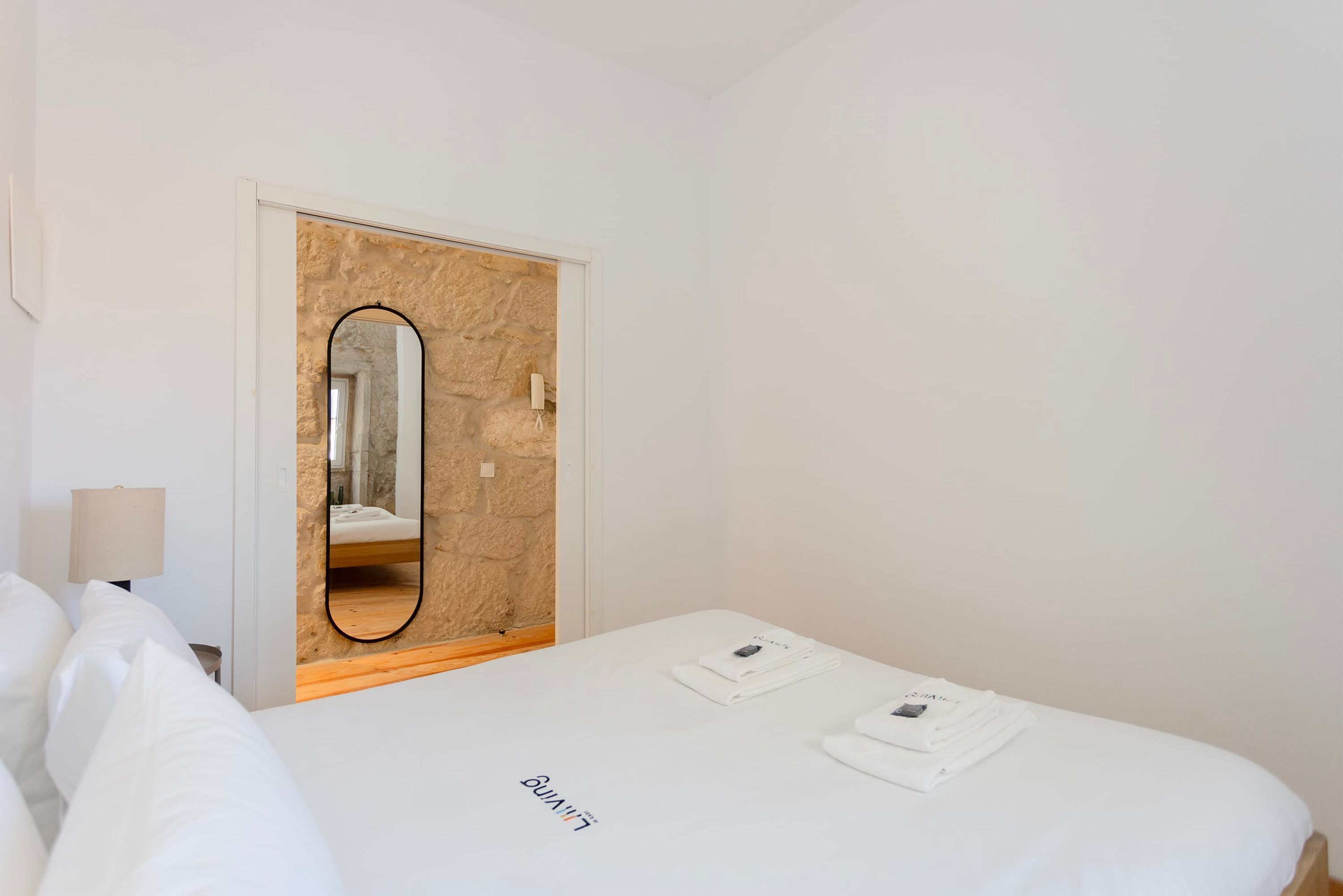 Habitación de hotel con una cama, un espejo, una lámpara y una puerta adosada a una pared de piedra.