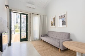 Uma sala de estar moderna com um sofá cinzento, uma mesa de centro de madeira e uma janela grande com cortinas.