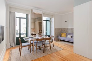 Uma sala de estar moderna com área de jantar, janelas amplas, um sofá e uma televisão.