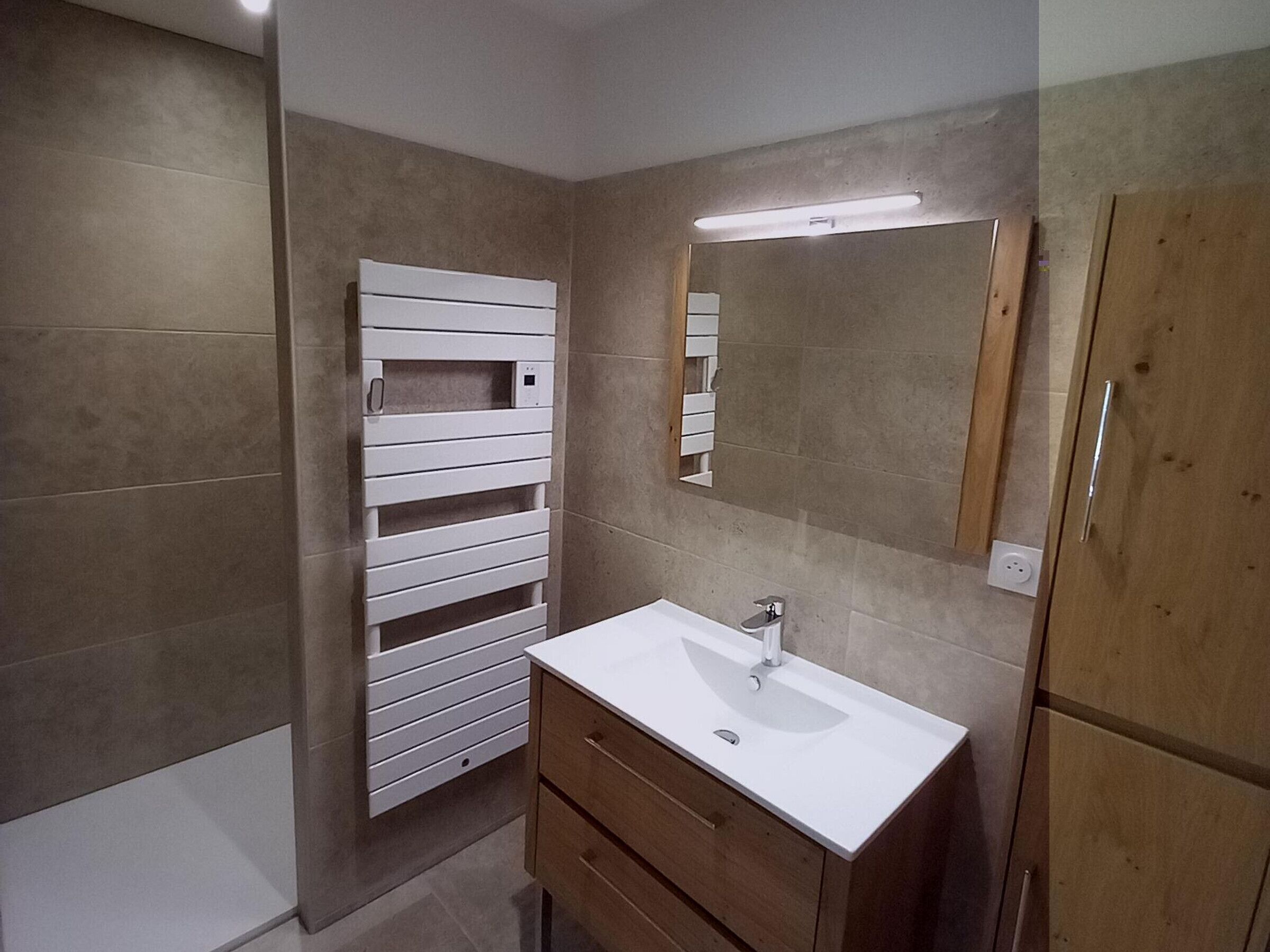 Un baño con lavamanos blanco, mueble de madera y un espejo.