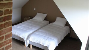 A bedroom with two beds, a brick wall, and a sloped ceiling. - Charming Countryside Home with Modern Amenities in Scenic Perche Hills (Melleray)
