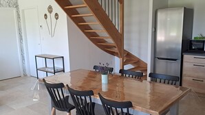 A modern kitchen with a wooden staircase, a dining table with chairs, and a stainless steel refrigerator. - Charming Countryside Home with Modern Amenities in Scenic Perche Hills (Melleray)