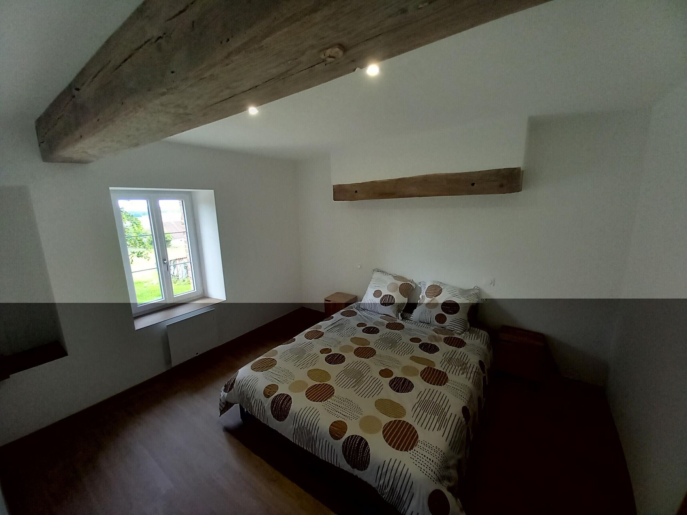 Une chambre à coucher avec un lit, une fenêtre et une poutre en bois au plafond.