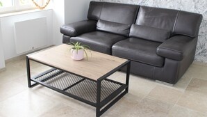 A black leather sofa, a wooden coffee table with a plant, and a patterned wallpaper. - Charming Countryside Home with Modern Amenities in Scenic Perche Hills (Melleray)