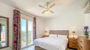 Ein Schlafzimmer mit einem großen Bett, einem Deckenventilator, einem Nachttisch mit Lampe und einer Kommode.