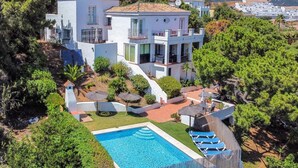 Eine moderne Villa mit Swimmingpool, umgeben von üppiger Vegetation und einer Bergkulisse.