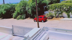 Zona residencial con un coche rojo estacionado en la calle, rodeada de vegetación y viviendas.