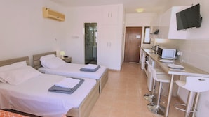 Habitación de hotel con dos camas, kitchenette, televisor y zona de ducha.