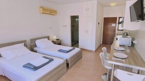 A hotel room with two beds, a small kitchenette, a shower, and a TV. - 49 AN- Nissi Heaven Studio (Ayia Napa)