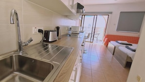 Cocina compacta con lavabo, tostadora, hervidor y zona de comedor con mesa y sillas.