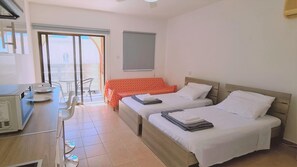 A hotel room with two beds, a desk with a computer, and a dining area with chairs. - 49 AN- Nissi Heaven Studio (Ayia Napa)