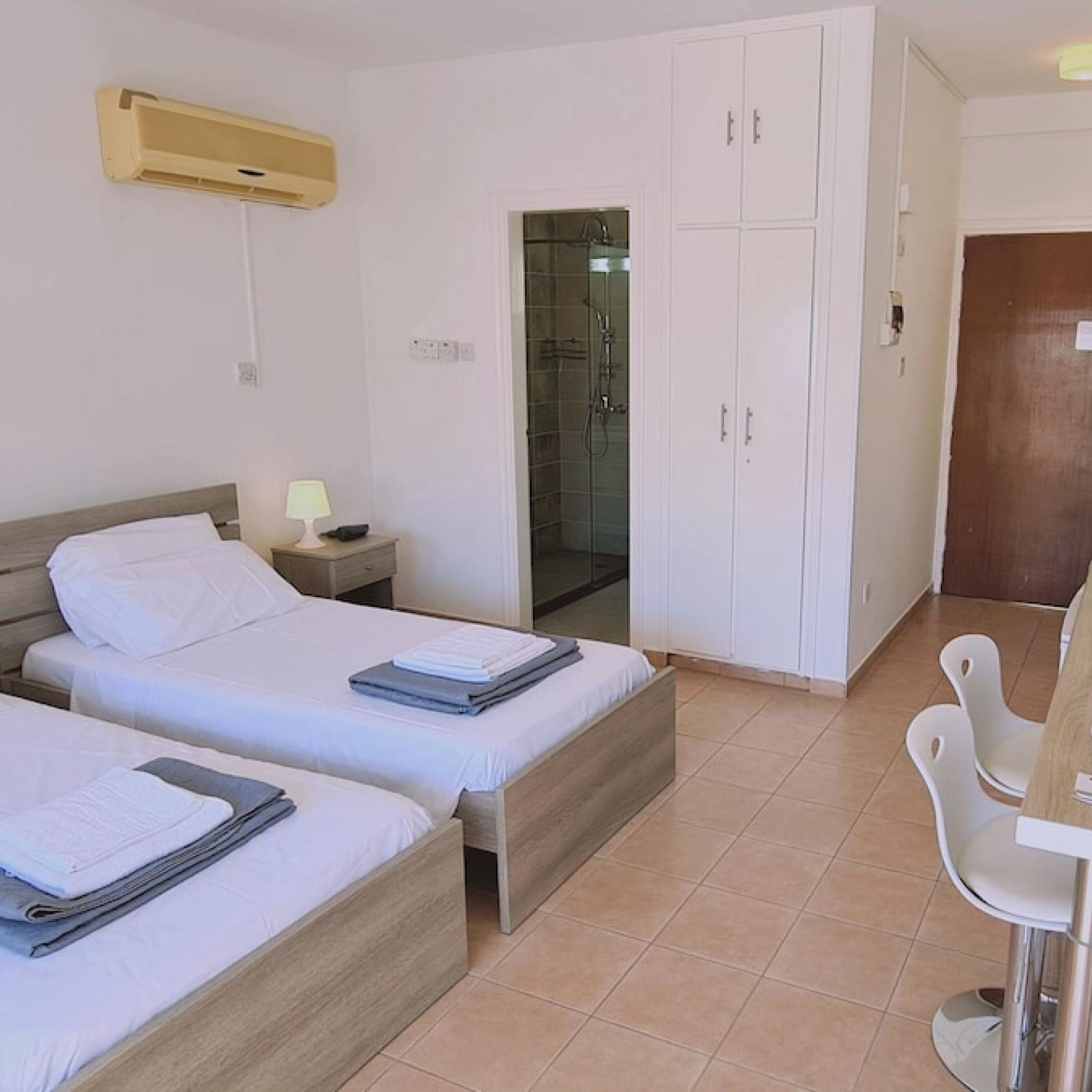 Habitación de hotel con dos camas, un escritorio, una silla, un armario y zona de ducha.