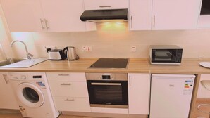 Una cocina compacta equipada con lavadora, horno Bosch, microondas y tostadora.