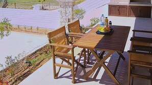 Une terrasse avec une table et des chaises, offrant une vue panoramique sur la mer et les champs.