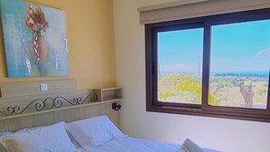 Un lit bien fait, avec du linge de lit et des serviettes blanches, un tableau accroché au mur et une fenêtre donnant sur un paysage.