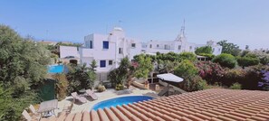 A rooftop pool area with lounge chairs and a small pool, surrounded by white buildings and greenery. - 15 ATH - Swallow s Nest Villa (Sotira)