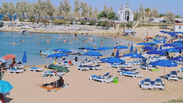 A beach with numerous sun loungers and umbrellas, a clear blue sky, and a few people swimming in the water. - 20 ATR -trinity 1 Apartment (Paralimni)
