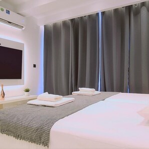 A modern hotel room with a large bed, a flat-screen TV, a bedside table with a bottle and glasses, and a window with dark curtains. - 116 AN 2 - Mezarina 2 Apartment (Ayia Napa)