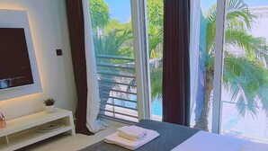A hotel room with two beds, a TV, a small table with a plant, and a view of palm trees and a pool.