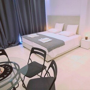 A neatly arranged bedroom with a bed, bedside tables, and a dining area with chairs. - 116 AN 2 - Mezarina 2 Apartment (Ayia Napa)