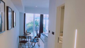 A modern hotel corridor with a dining area featuring a table and chairs, large windows with curtains, and a view of greenery outside.