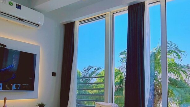 A hotel room with a bed, a TV mounted on the wall, and large windows with curtains.