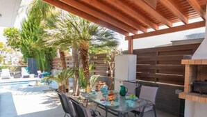 Eine Terrasse im Freien mit einem Glastisch, Metallstühlen und einem Grill.