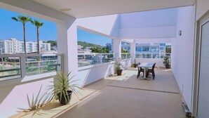 A balcony with a table and chairs, potted plants, and a view of buildings and palm trees. - 40 PRO 2 - Sunrise Beach Apt 2 (Paralimni)