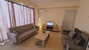 A living room with a sofa, a coffee table, and a TV on a wooden stand. - 40 PRO 2 - Sunrise Beach Apt 2 (Paralimni)