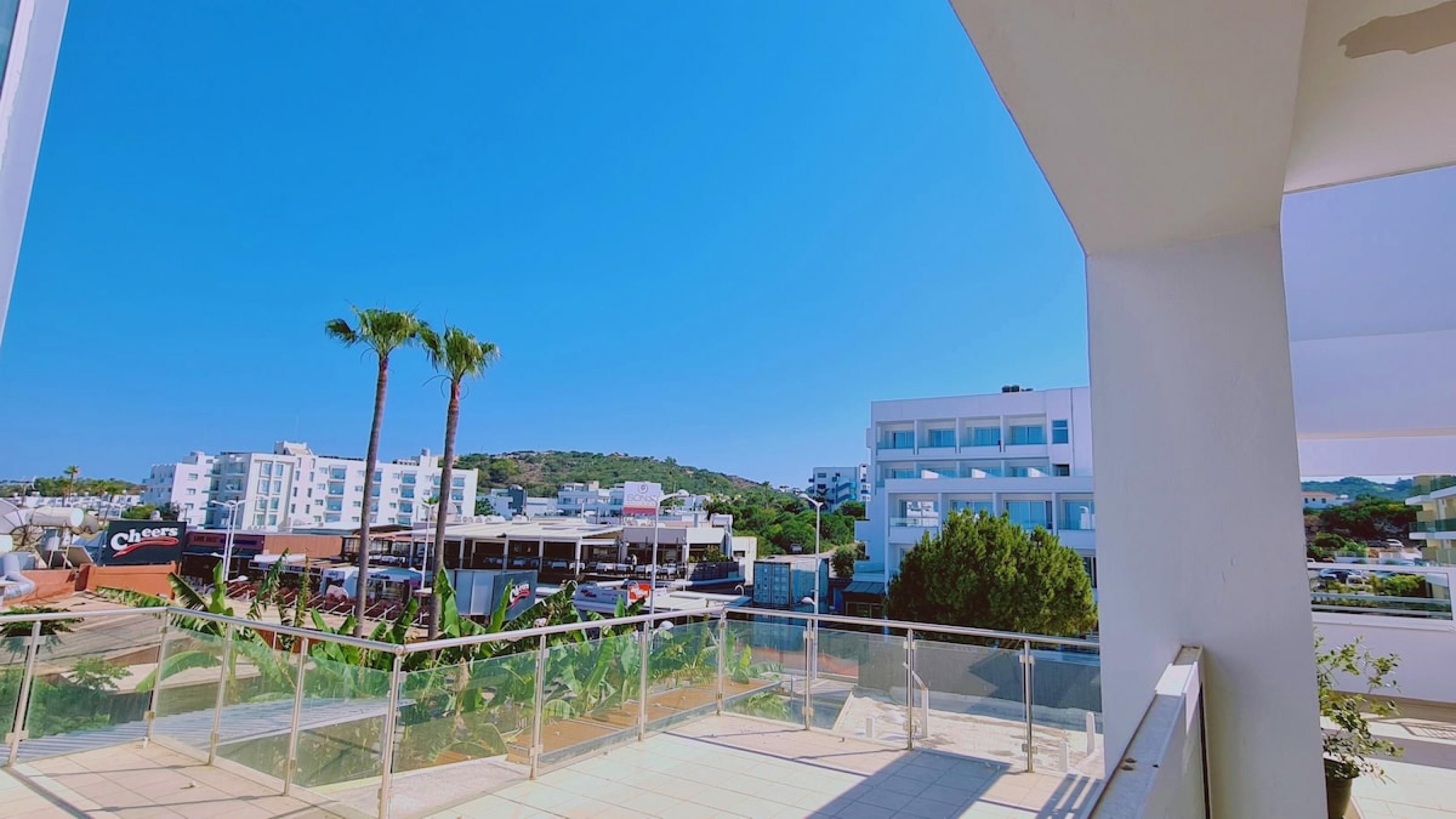 A balcony with a clear view of a cityscape, including modern buildings and palm trees.