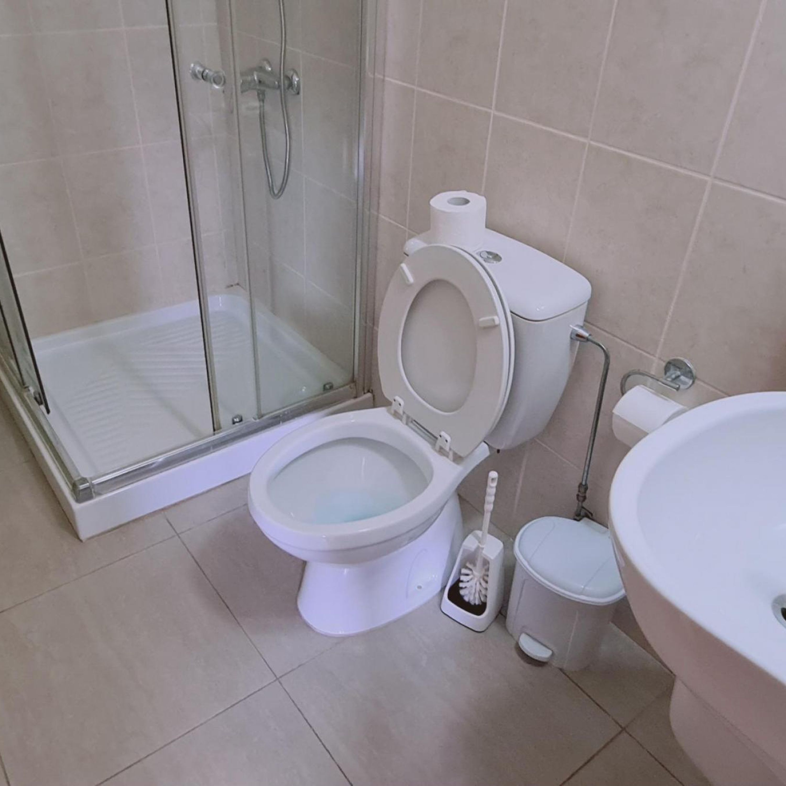 A modern bathroom with a glass-enclosed shower, a toilet, and a sink.