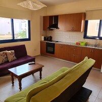 Una sala de estar con sofá y mesa de centro, una cocina con muebles de madera y un ventanal, y vistas al exterior.