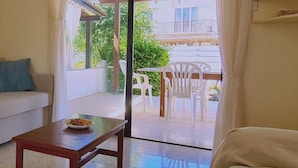 Une pièce comprenant un canapé, une table avec une assiette de nourriture, et donnant sur un balcon extérieur avec des chaises et une table.