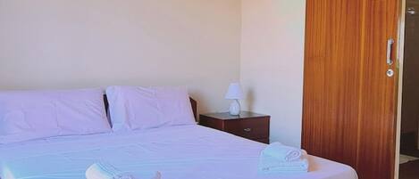 A bedroom with a bed, pillows, a nightstand, a lamp, and a wooden wardrobe.