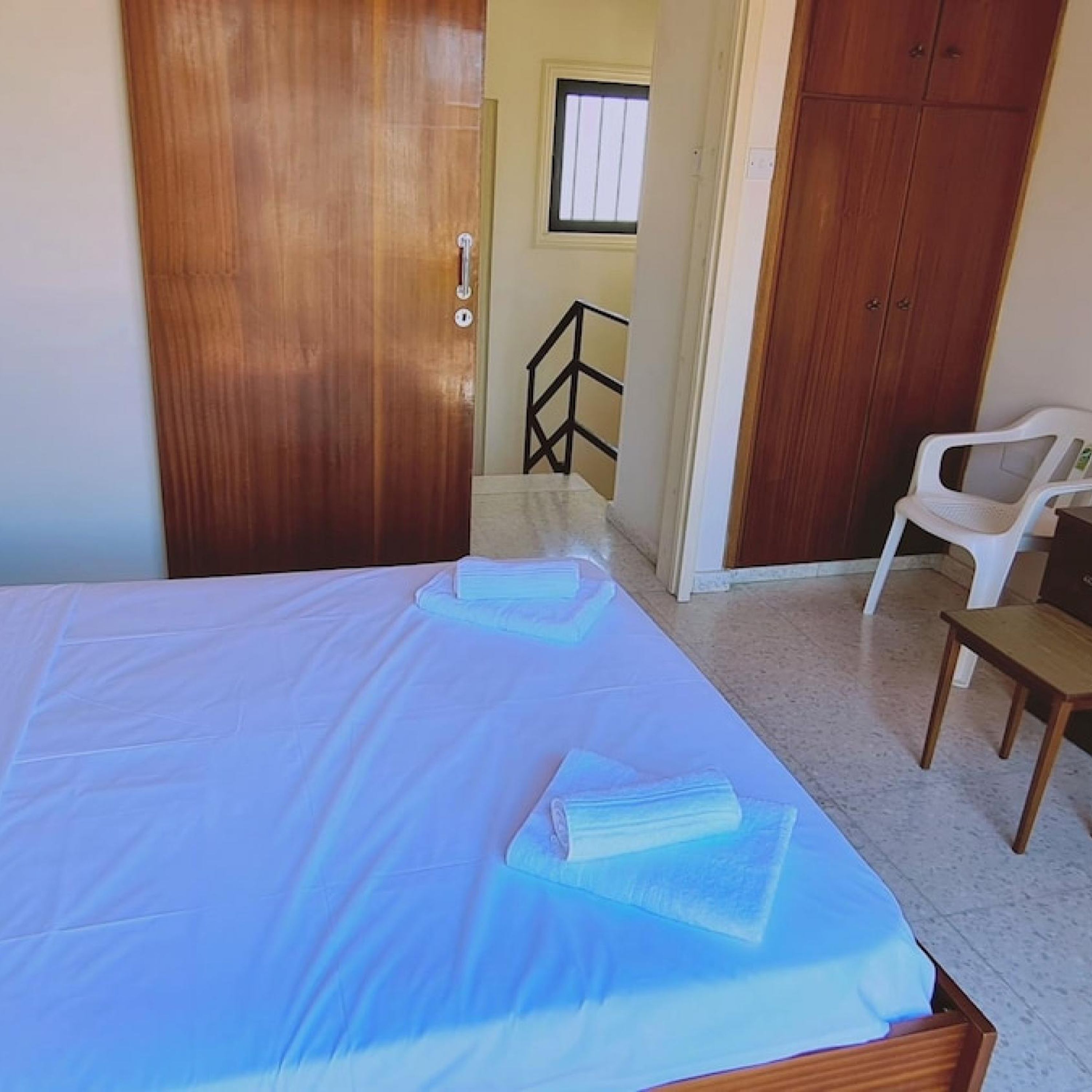 A bedroom with a wooden bed, a white chair, and a wooden desk.