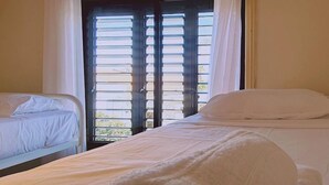 Une chambre d’hôtel avec deux lits, une grande fenêtre avec des stores et une vue sur la verdure.