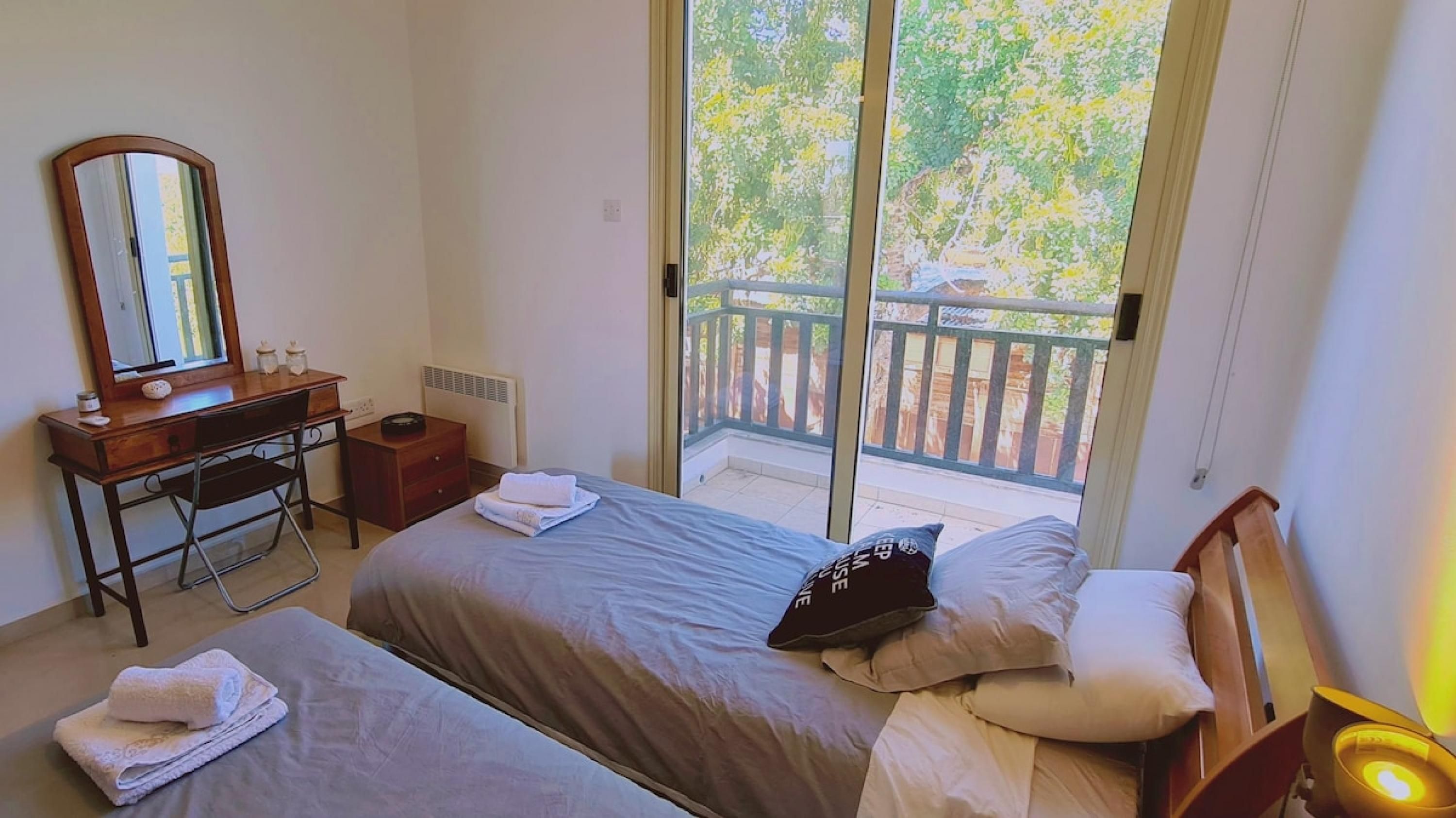 Un dormitorio con dos camas, un aparador, un espejo y un balcón con vistas a árboles.