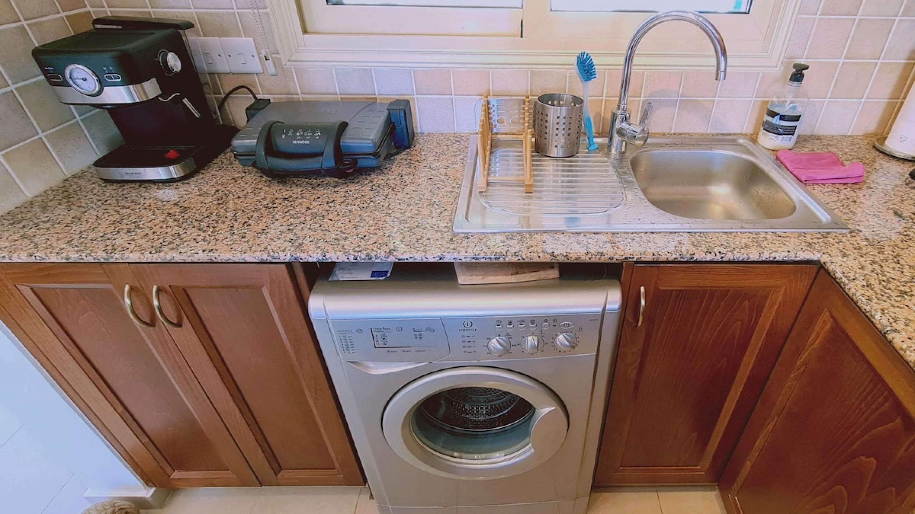 A kitchen with a washing machine, a coffee maker, a toaster, a sink, and a dish rack.