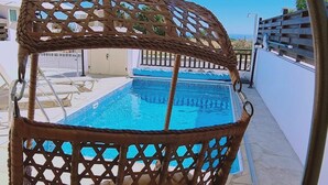 A wicker swing chair with a view of a swimming pool. - 47 PEY - Peyia Kamelia Villa (Pegeia)