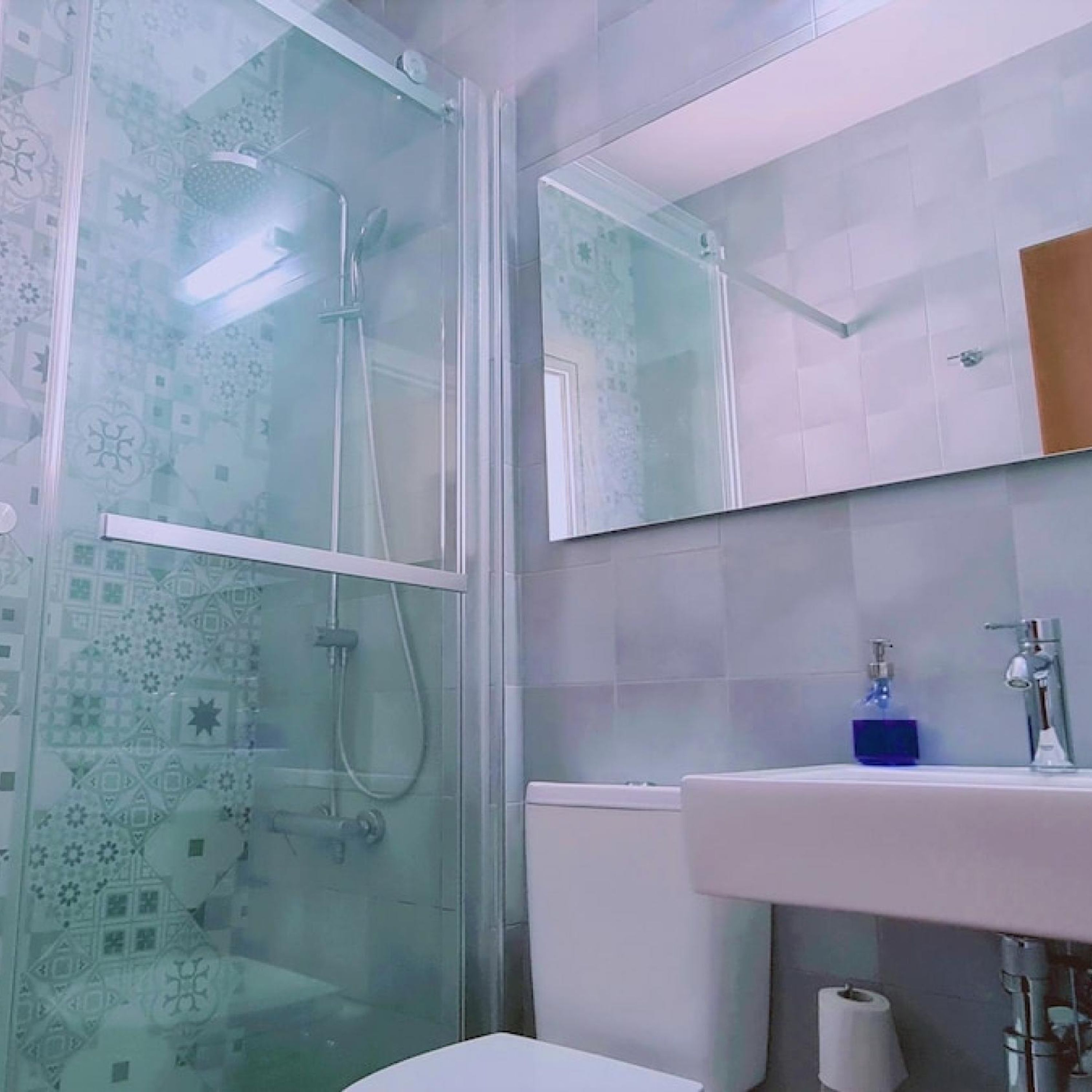 A bathroom with a glass shower enclosure, a white sink, and a mirror above the sink.