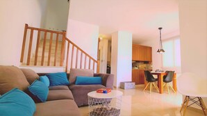 A living room with a sofa, coffee table, and a dining area with chairs and a table. - 47 PEY - Peyia Kamelia Villa (Pegeia)