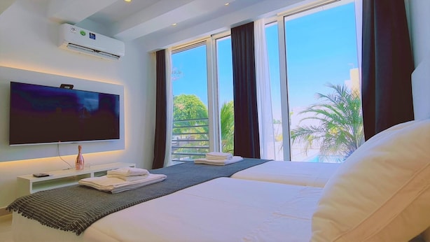 A hotel room with a bed, a TV, a small table with a bottle, and a window with curtains. - 116 AN 1 - Mezarina 1 Apartment (Ayia Napa)