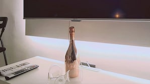 A television displaying the Netflix logo, a remote control, and a bottle of champagne on a white surface. - 116 AN 1 - Mezarina 1 Apartment (Ayia Napa)