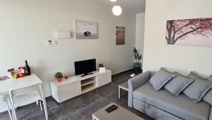 Una sala de estar moderna con un sofá gris, un televisor de pantalla plana, una mesa de comedor con sillas y obras de arte en las paredes.
